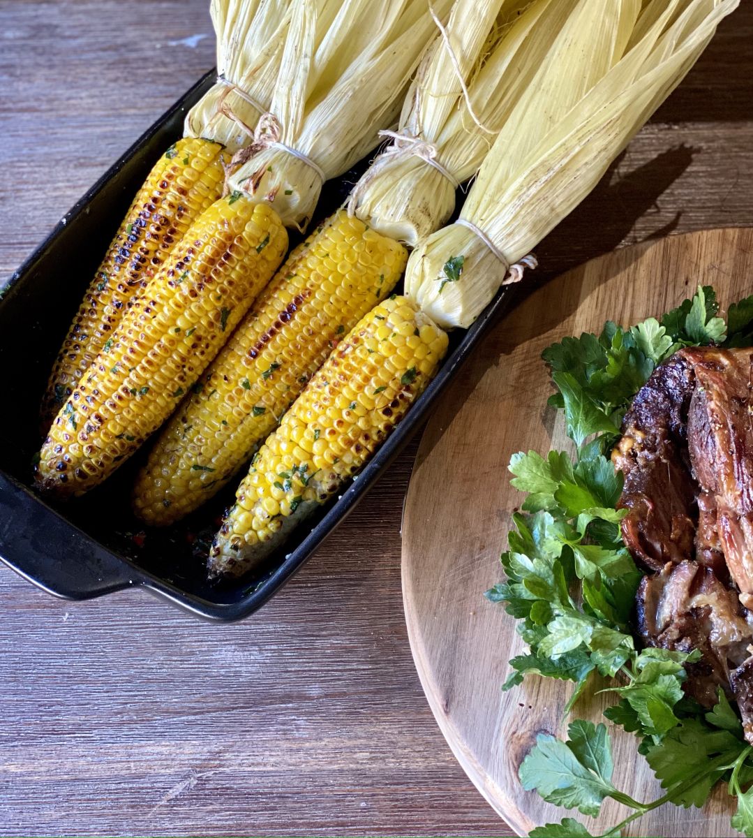 Cobs of corn charred on the BBQ with butter, garlic and parsley