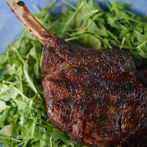 A tomahawk steak that's been cooked on a BBQ on a bed of rocket leaves