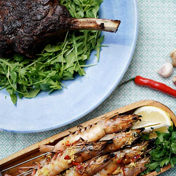 A wooden tray with barbequed prawns and a tomahawk steak with rocket salad.