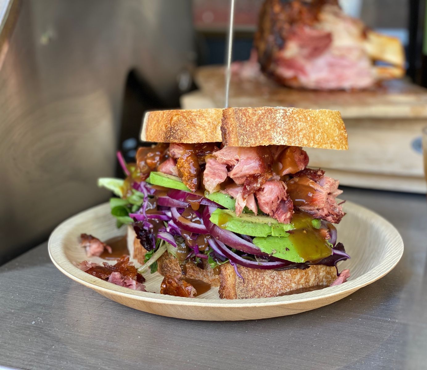 A sandwich with BBQ pork knuckle, avocado, salad, Spanish onion and red cabbage on an outdoor kitchen BBQ