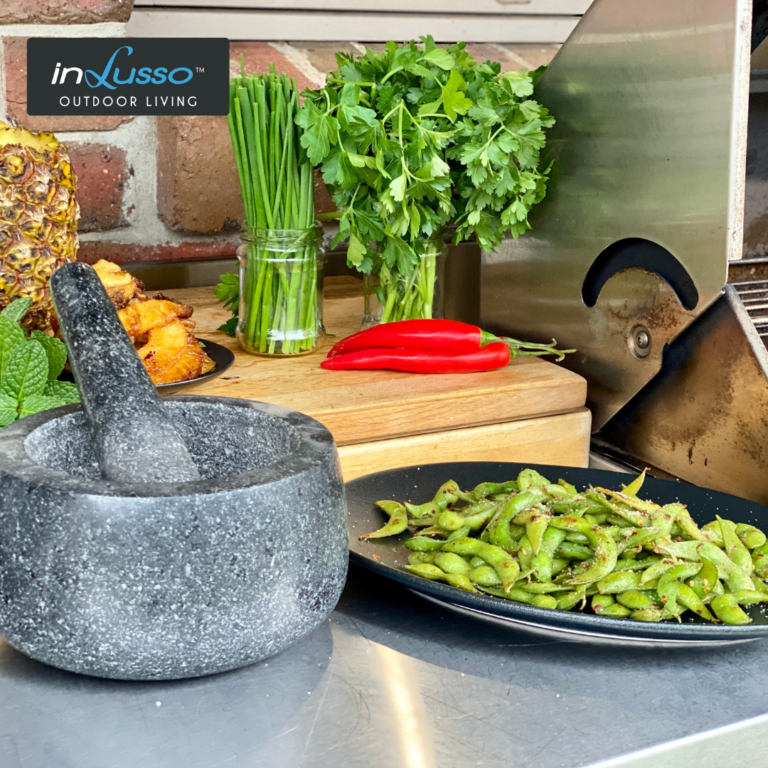 An outdoor BBQ kitchen with mortar and pestle, herbs and chilli salt edamame