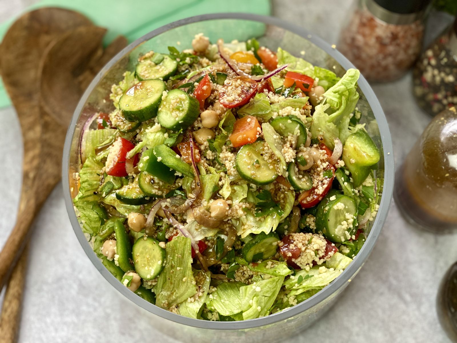 couscous and salad ingredients in a glass bowl with servers