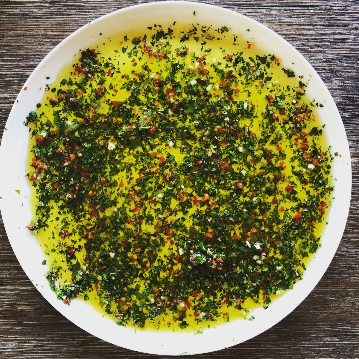 A fresh marinade of olive oil, herbs, chilli and salt and pepper in a large white bowl
