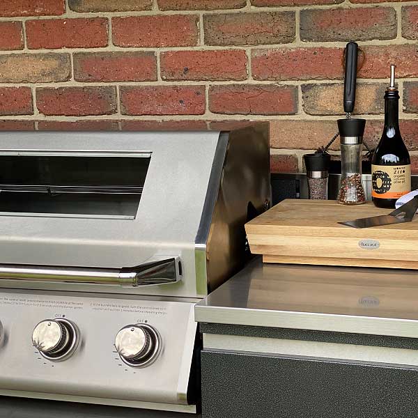 A stainless steel BBQ with hood, bench top, draws, chopping board and oil.