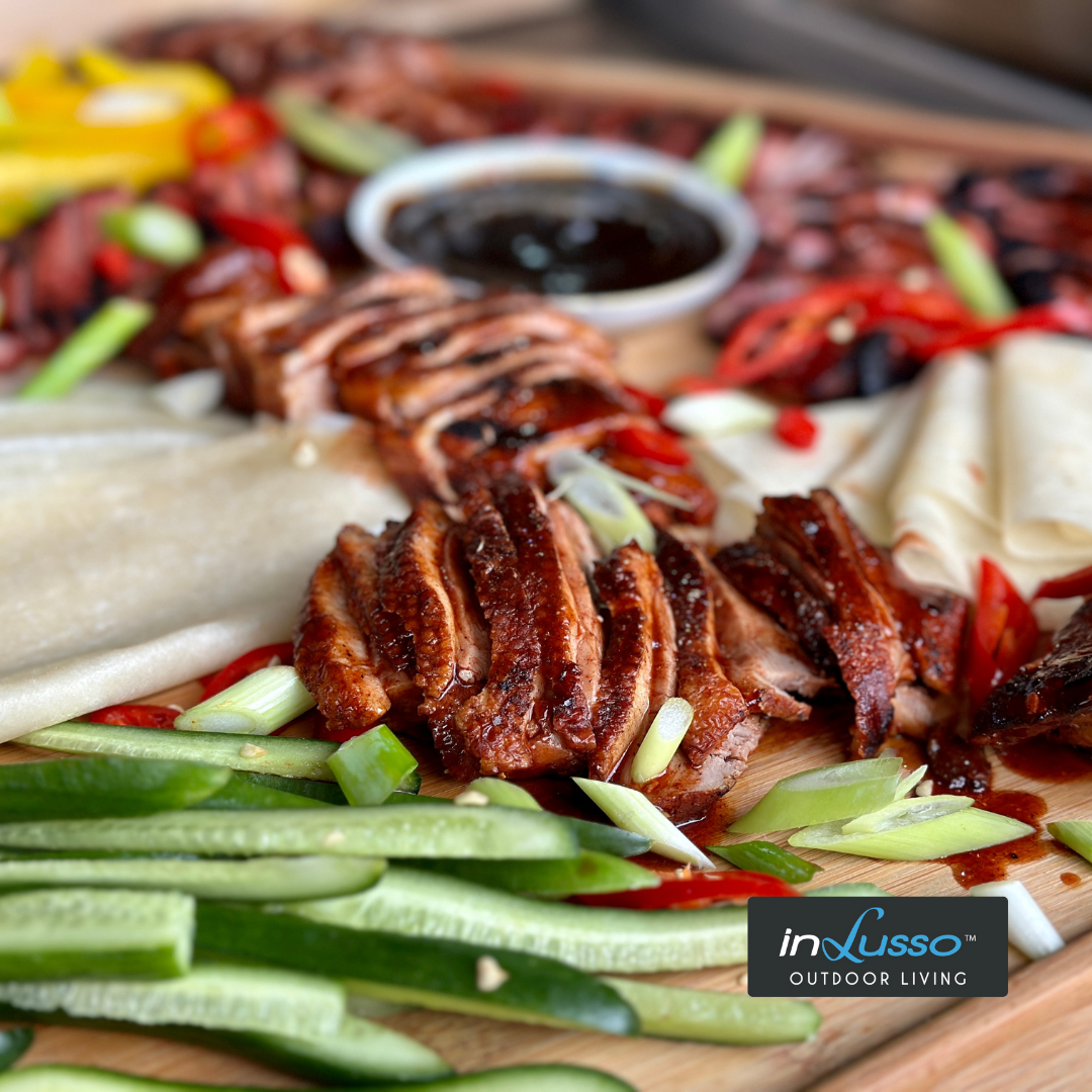 A platter on an outdoor kitchen with barbecued duck breast and pancakes