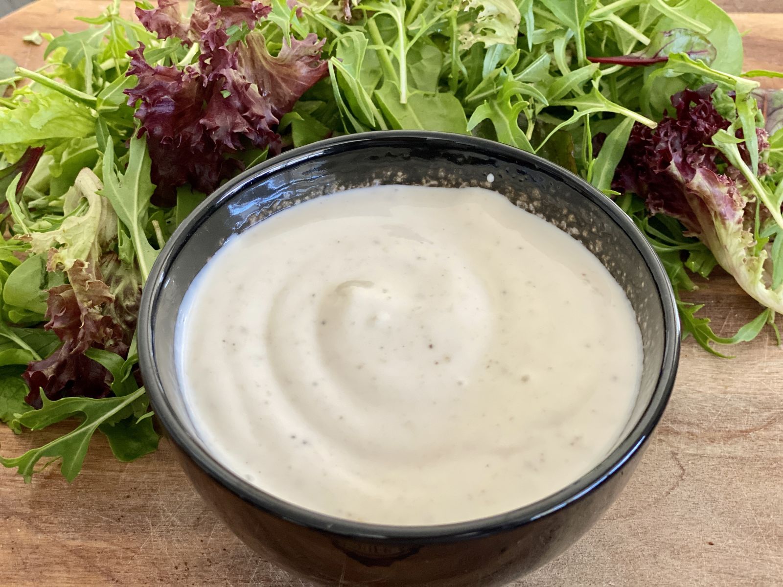 A yoghurt dipping sauce on a board with mixed lettuce leaves.